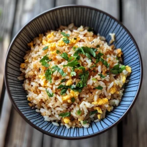A white bowl filled with golden egg fried rice, colorful vegetables, and sliced green onions, served on a rustic wooden table.