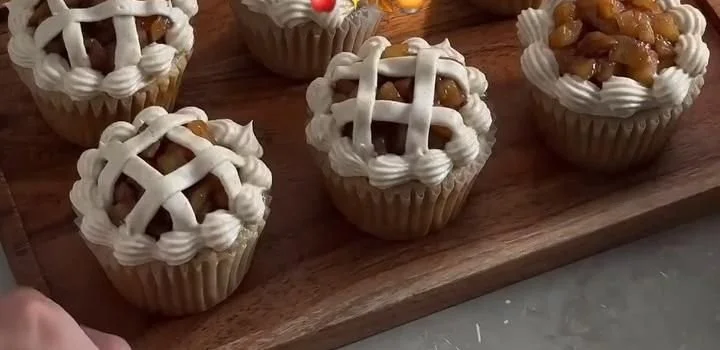 Delicious apple pie cupcakes topped with cinnamon frosting on a rustic wooden table
