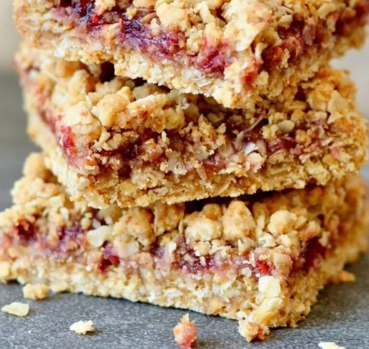 Homemade berry oat bars stacked on a cutting board with fresh berries on the side.