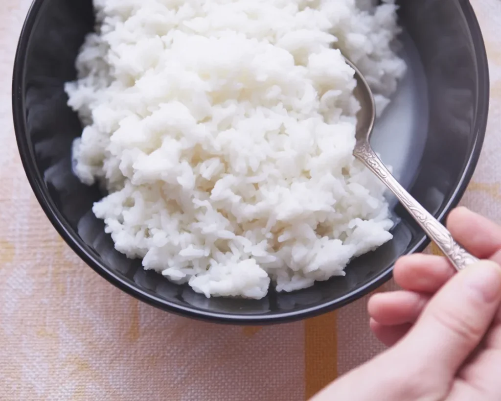 Cooked fluffy white rice in a pot with water and steam.