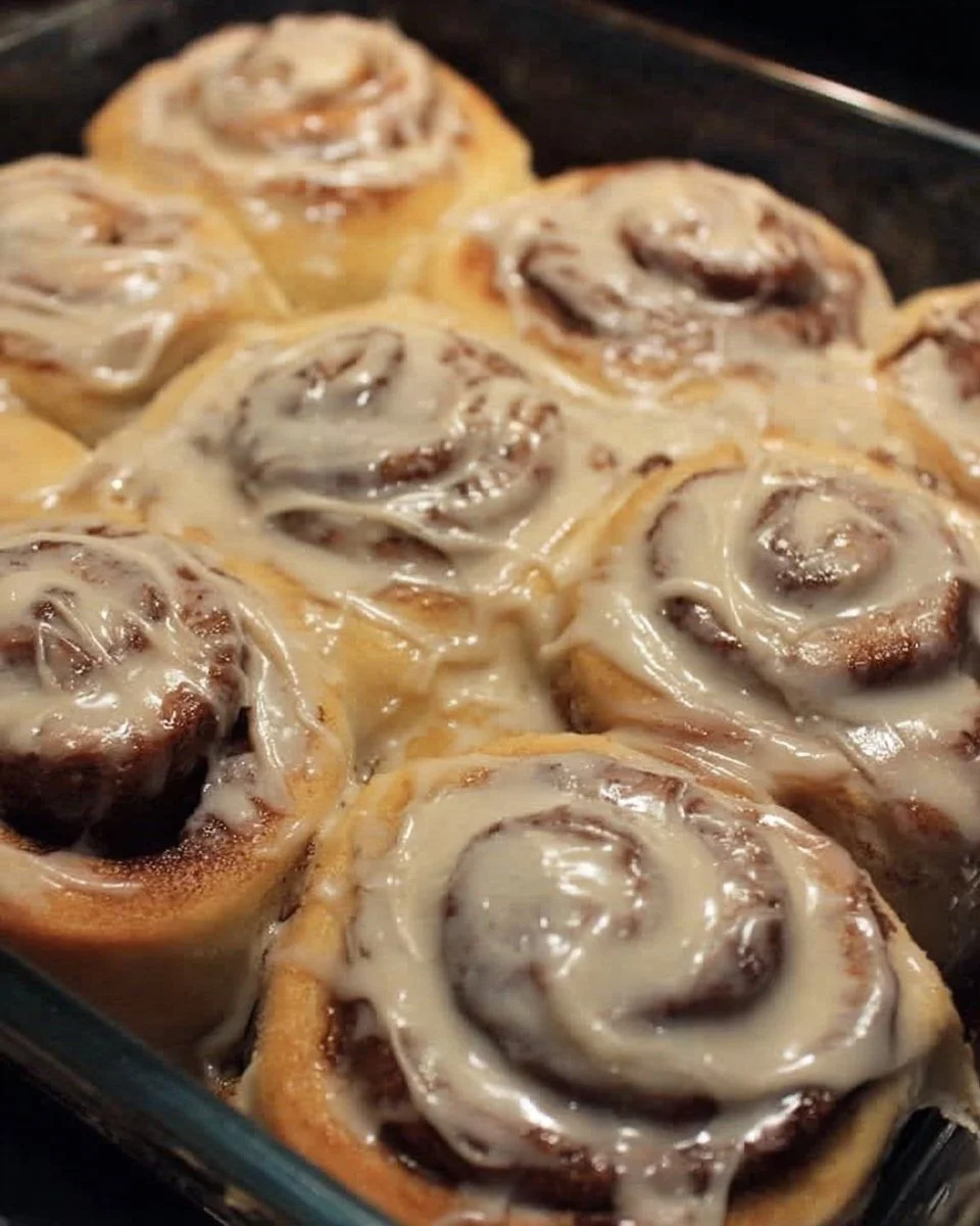 Homemade cinnamon rolls drizzled with brown butter frosting on a plate.