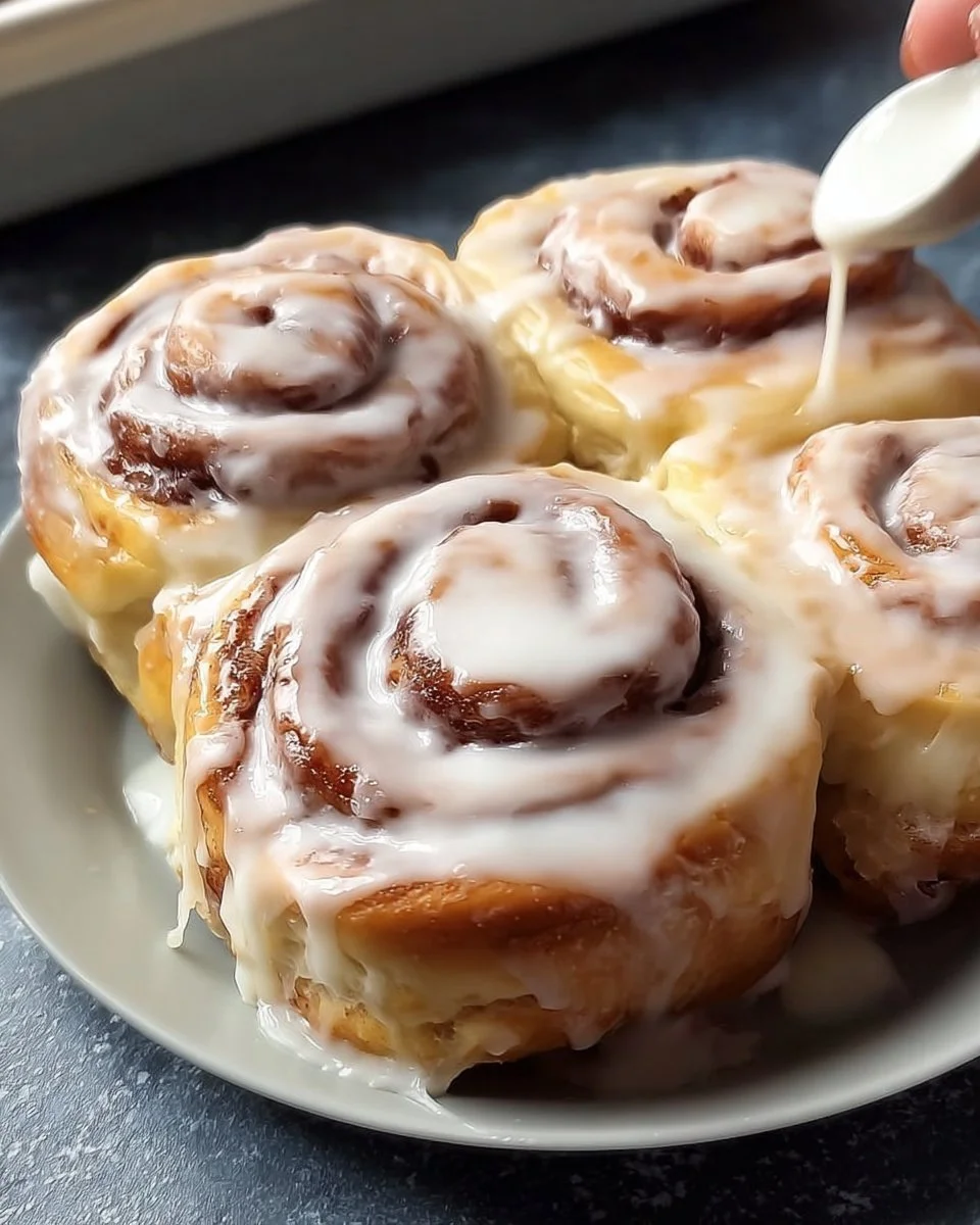 Homemade cinnamon rolls topped with icing on a rustic wooden table