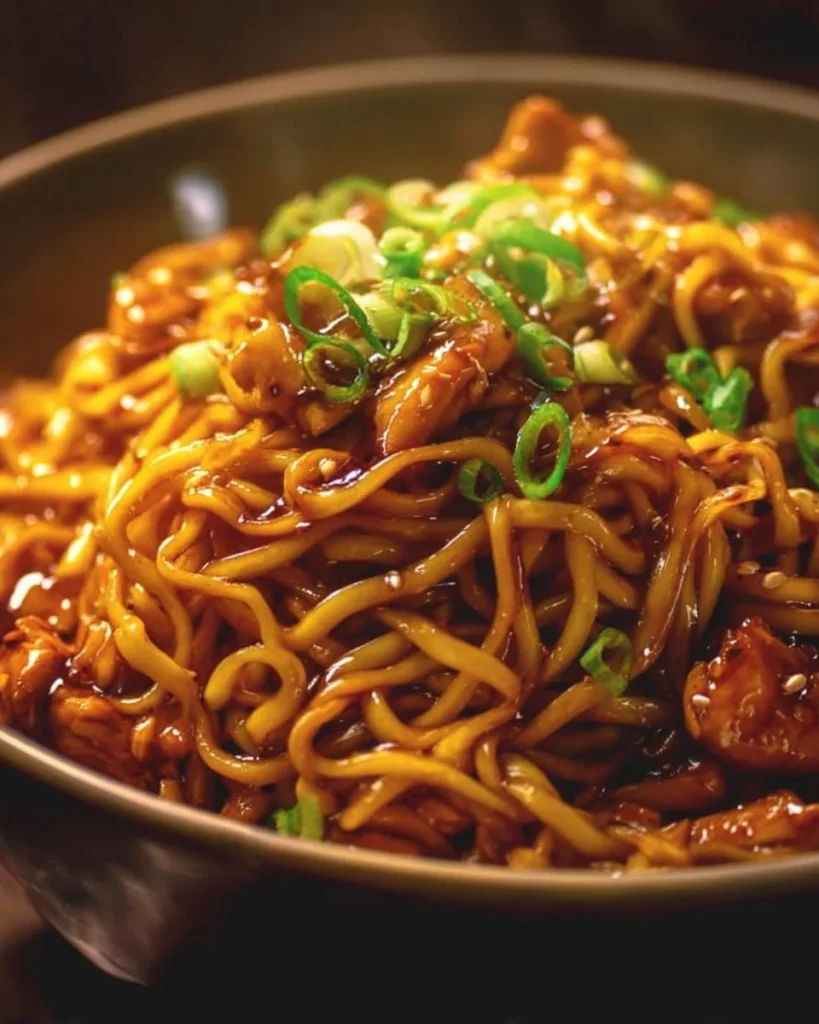 Plate of sticky garlic chicken noodles garnished with green onions